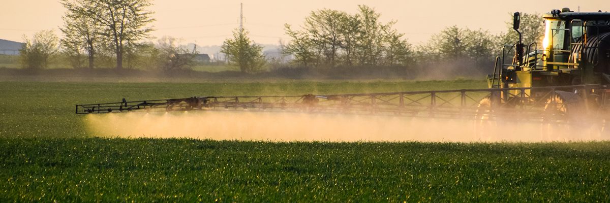Spring crop protection planning — tractor applying first spray treatment on a green field at sunset